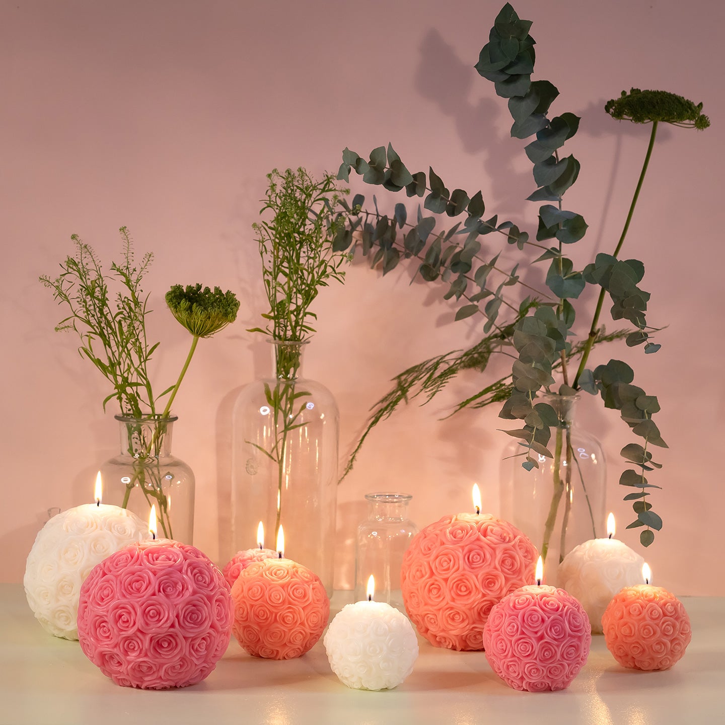 Bougies en forme de boules de roses allumées avec un décor de bocaux et de plantes